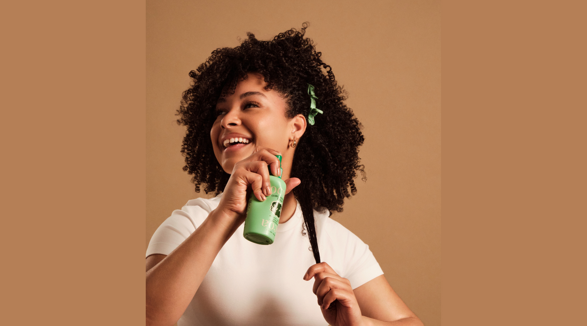 Woman with curly hair holding a green Ocoa spray bottle